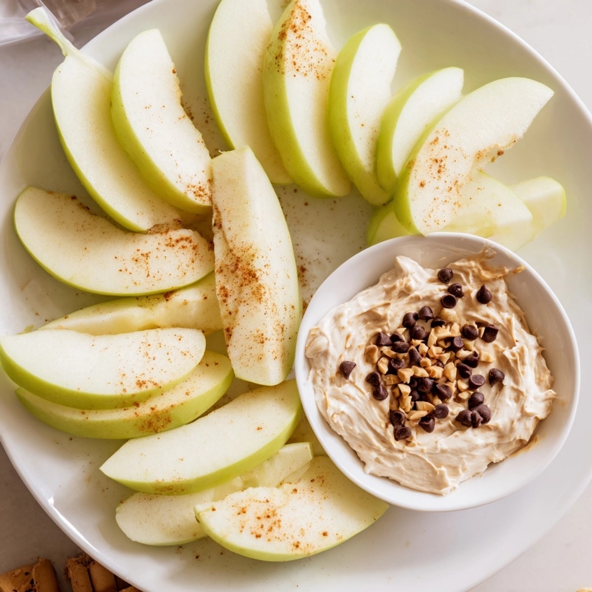 Close-up of juicy apple dippers with peanut butter, sprinkled with chopped peanuts and mini chocolate chips.