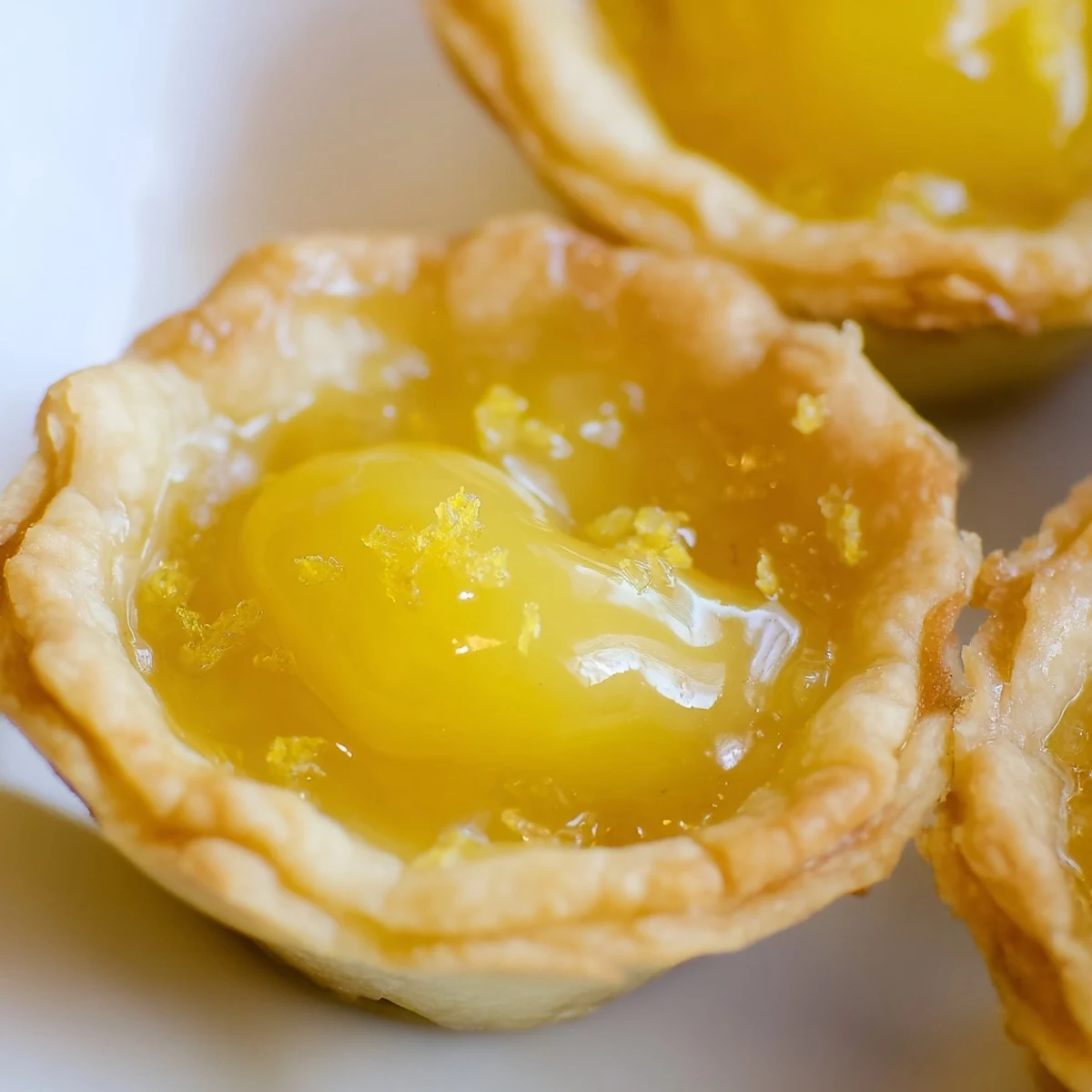 Twelve golden Lemon Curd Tartlets baked in a mini muffin tin, ready to be filled.