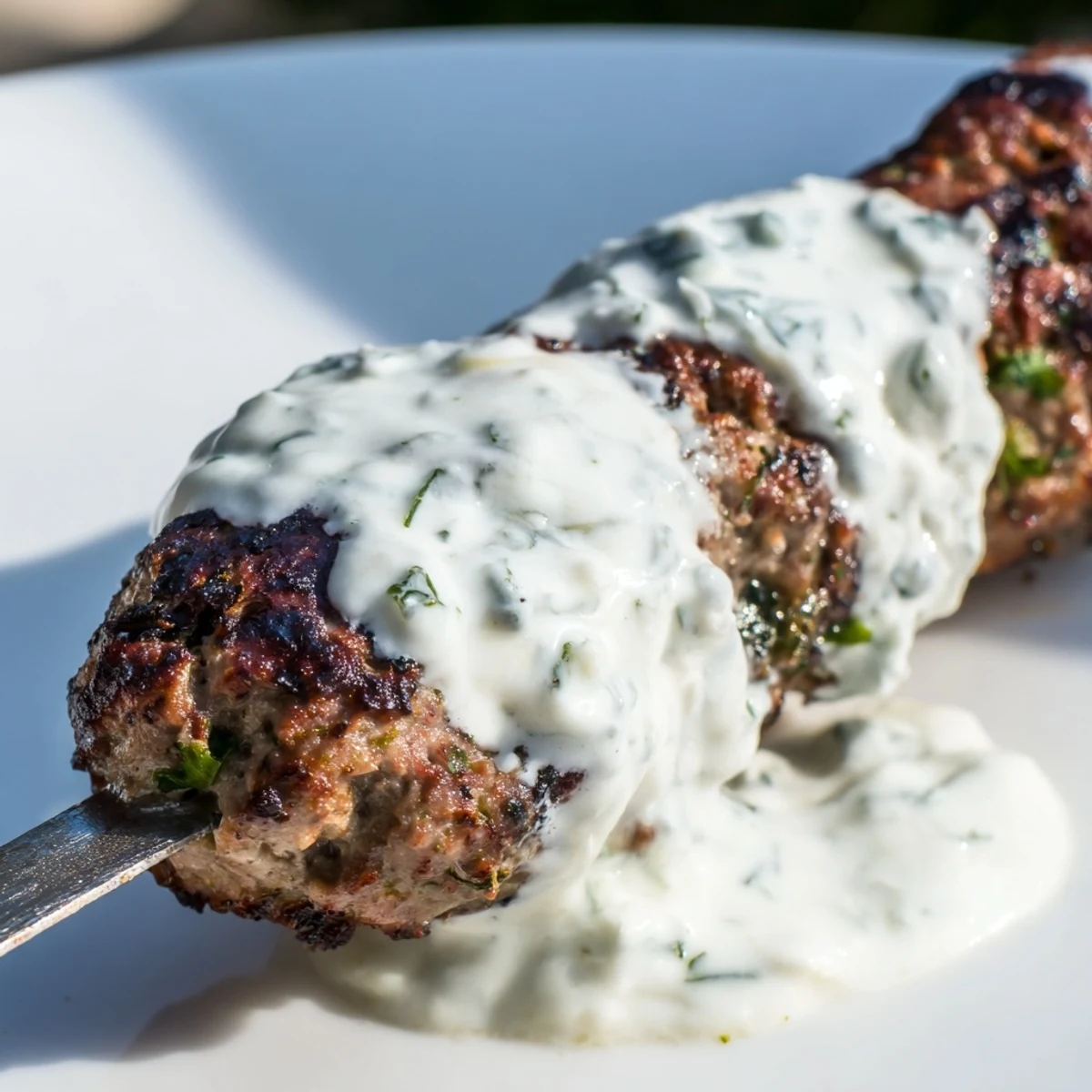 Tender, herb-packed Beef Kofta Kebabs with Tzatziki Sauce plated alongside crisp cucumbers, red onions, and fresh lemon wedges.