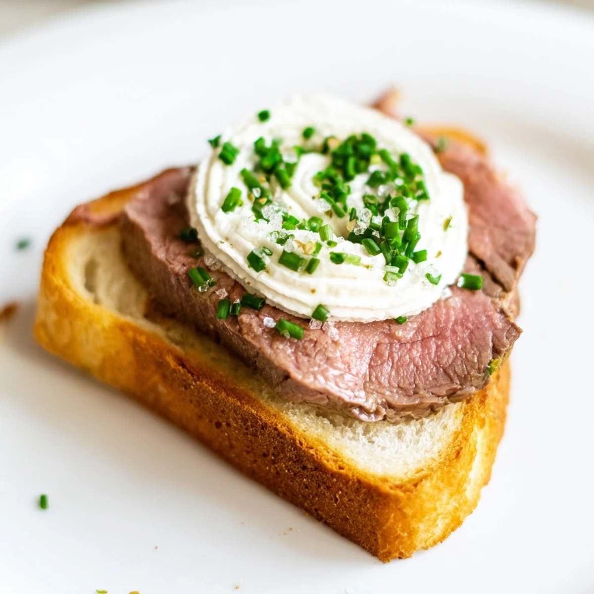 Savory beef toast points served warm on a plate, garnished with fresh chives for a light lunch.