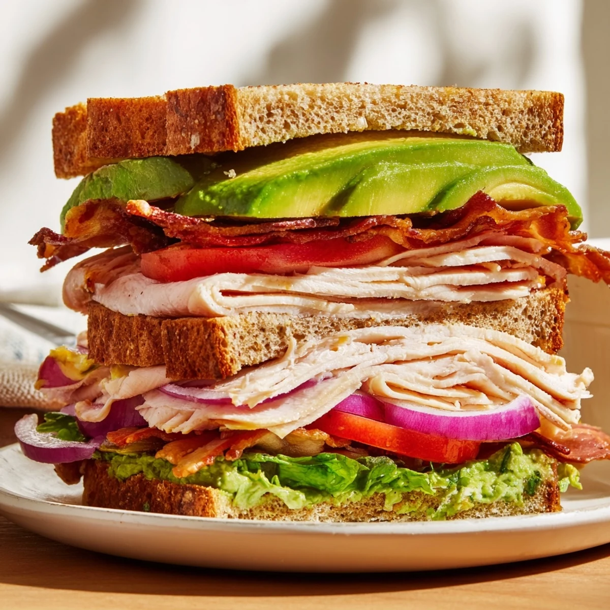 Triple-decker Turkey Club Sandwich stacked with crispy turkey bacon, creamy avocado, and fresh lettuce and tomato.
