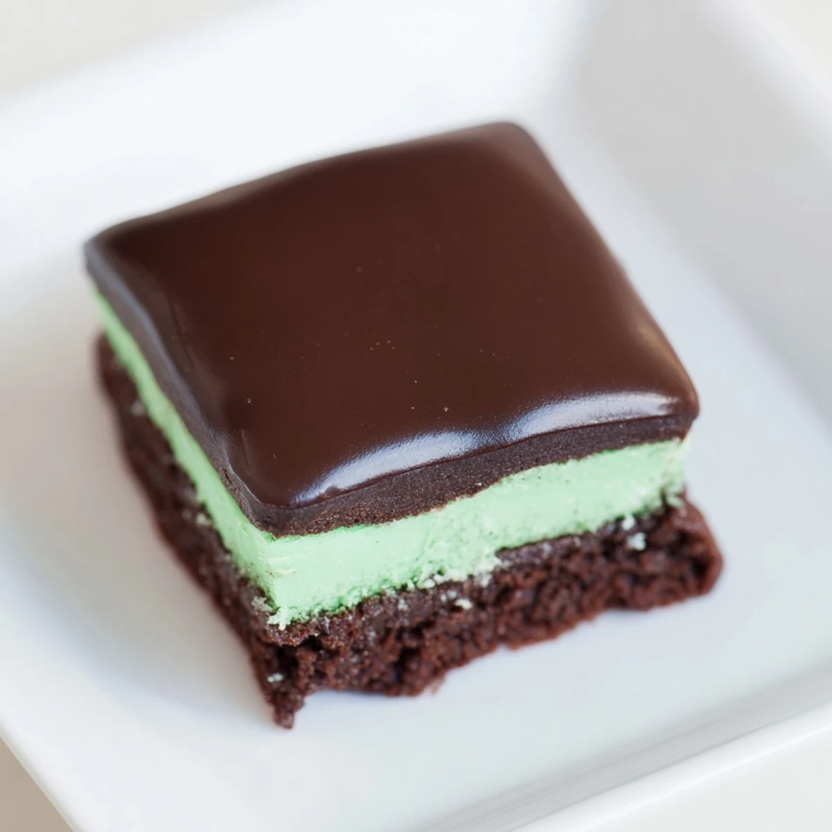 Freshly baked green mint brownies with a smooth ganache glaze, served on a rustic wooden board.  