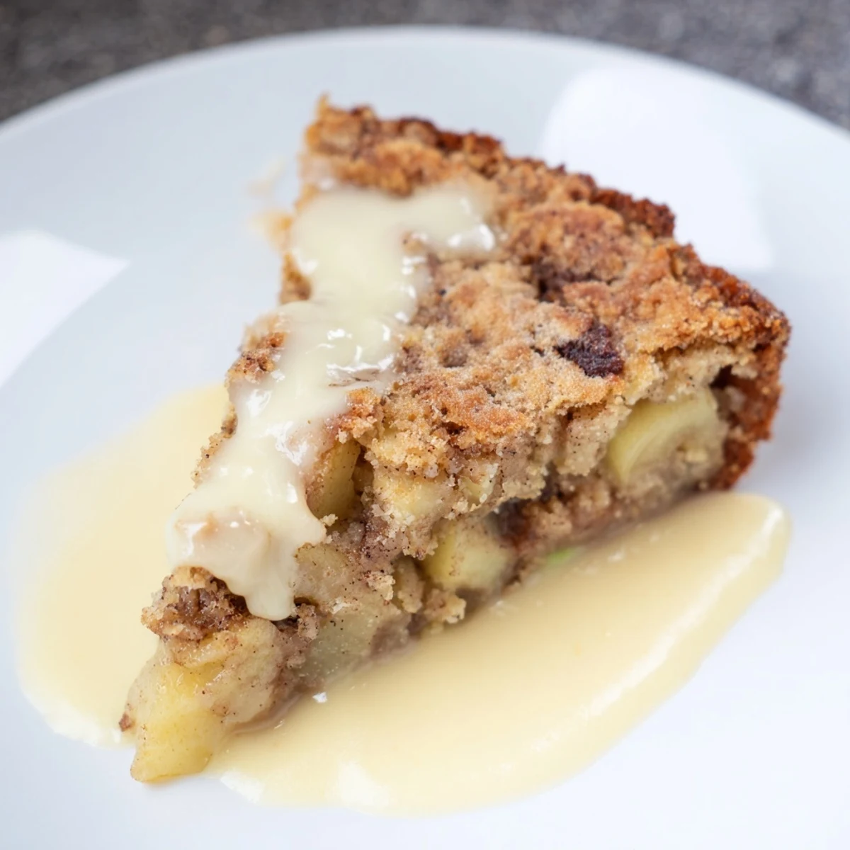 A slice of Irish Apple Cake with Custard rests beside a teacup, showcasing warm, creamy custard.