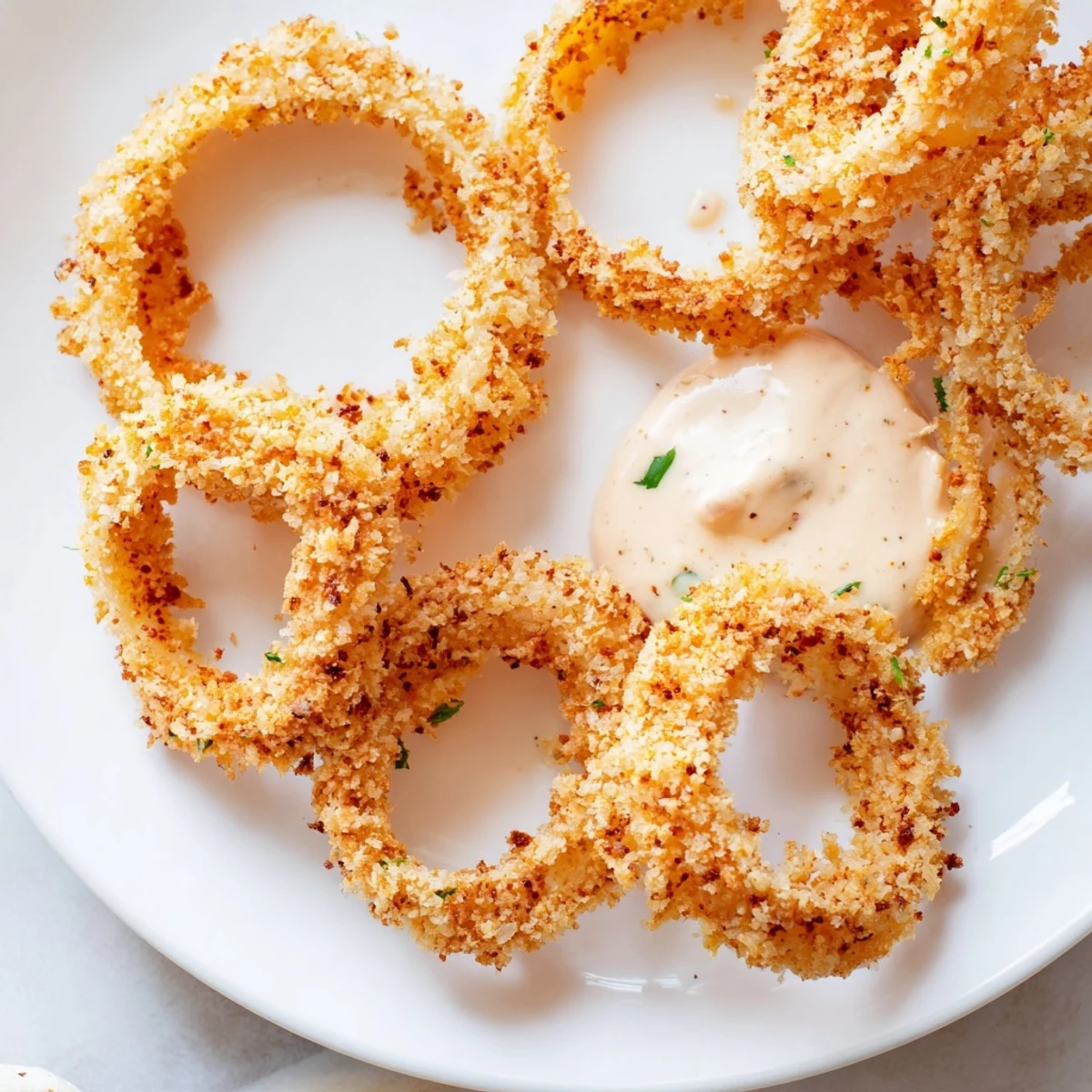 Freshly air-fried onion rings with crunchy panko coating and creamy chipotle mayo, perfect for a party appetizer tray.
