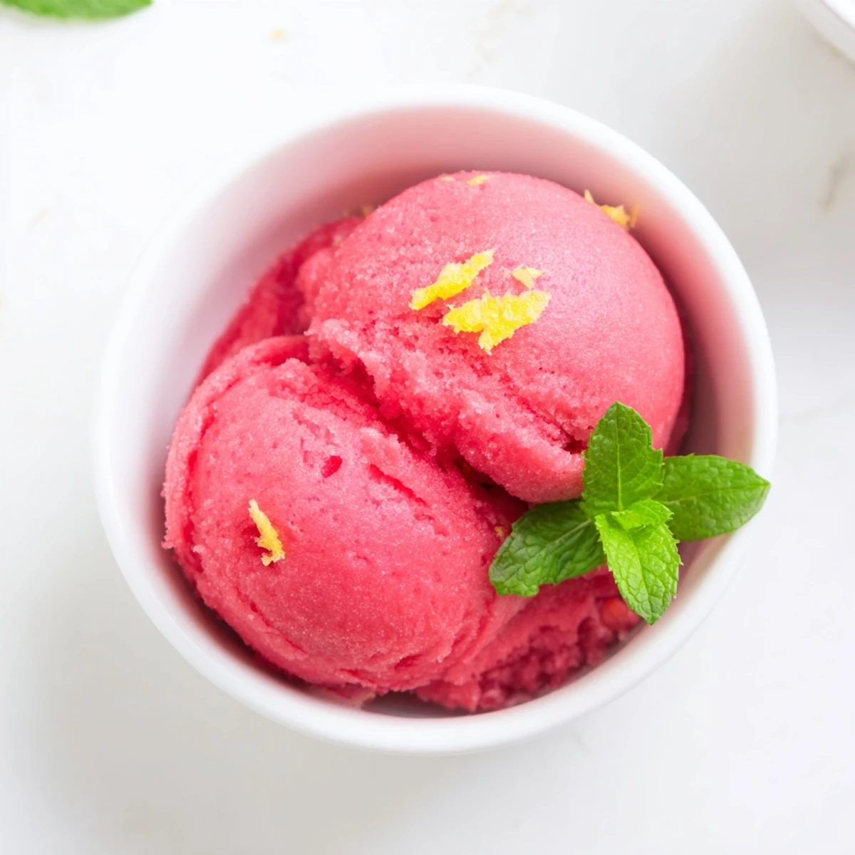 Serving suggestion for Pink Raspberry Lemonade Sorbet with Mint in a chilled glass, topped with a sprig of mint for summer dessert.