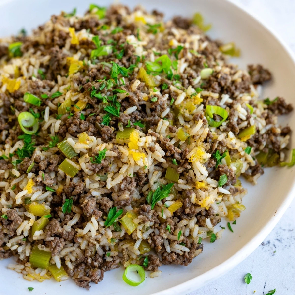 Cajun Dirty Rice with Ground Beef simmered in a skillet with aromatic vegetables, garnished with fresh parsley and green onions.