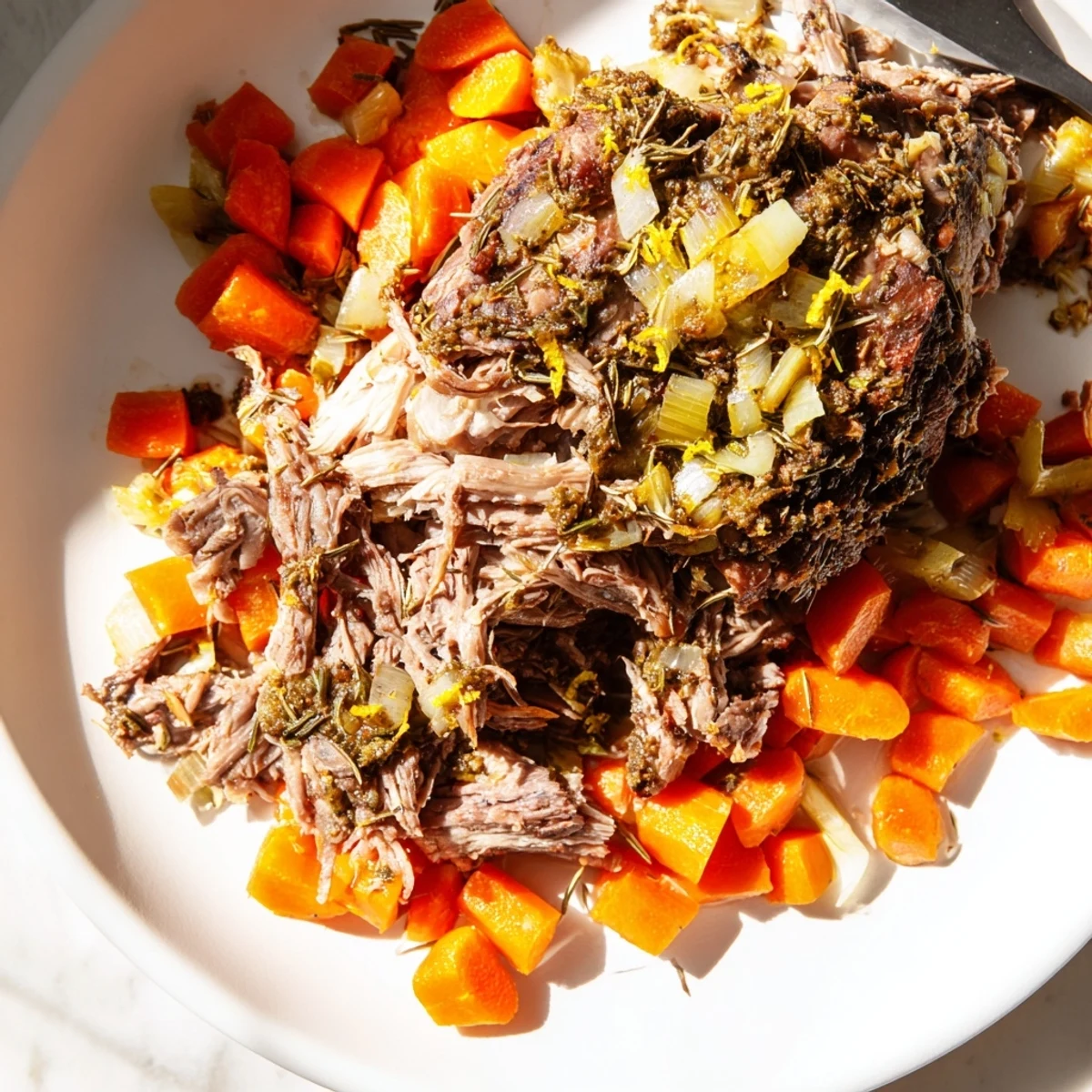 An appealing plate of Slow Cooked Lamb Shoulder with Garlic and Herbs served with carrots and onions, ready for a family dinner.