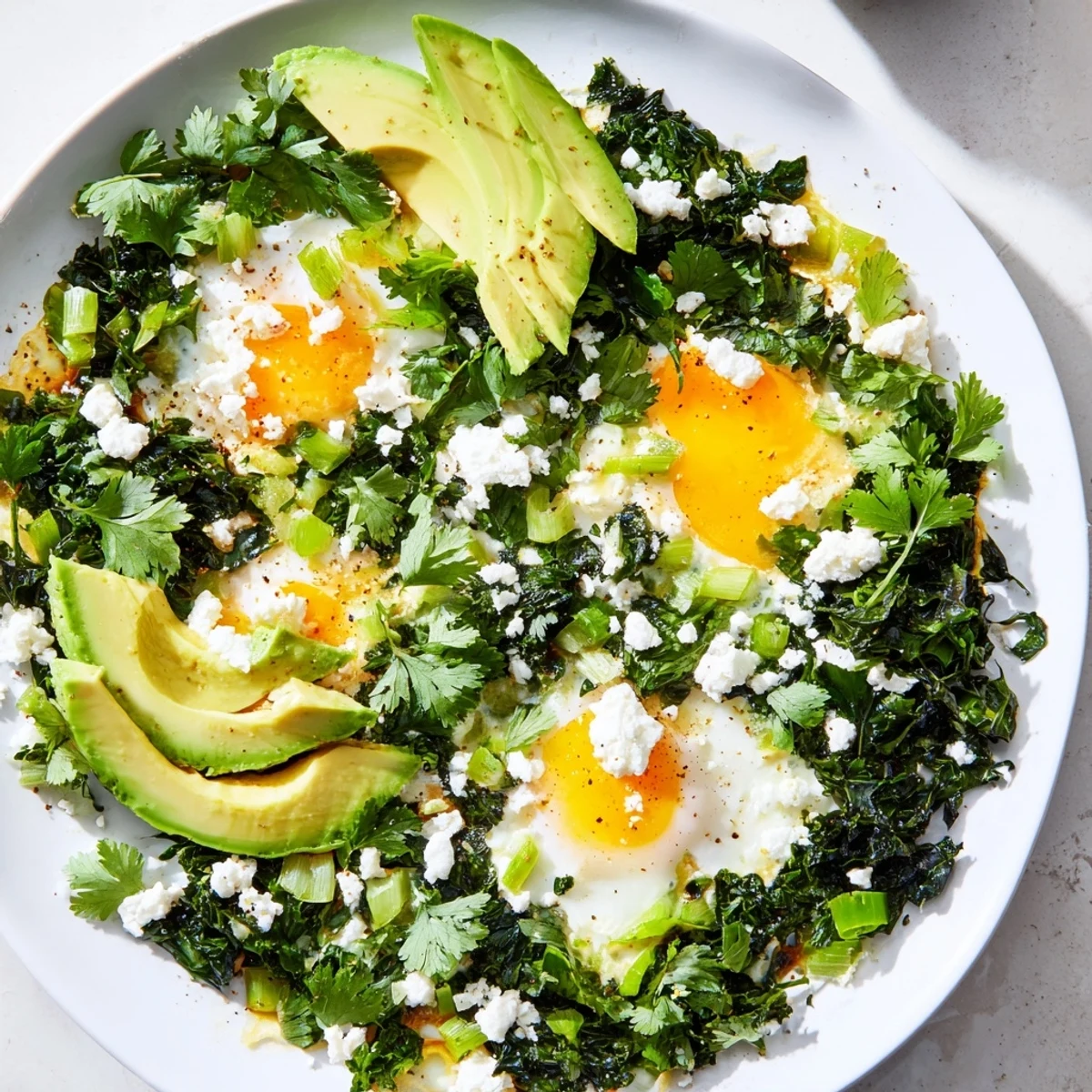 Green Shakshuka with Spinach and Feta served in a cast-iron pan topped with sliced avocado and fresh herbs.  