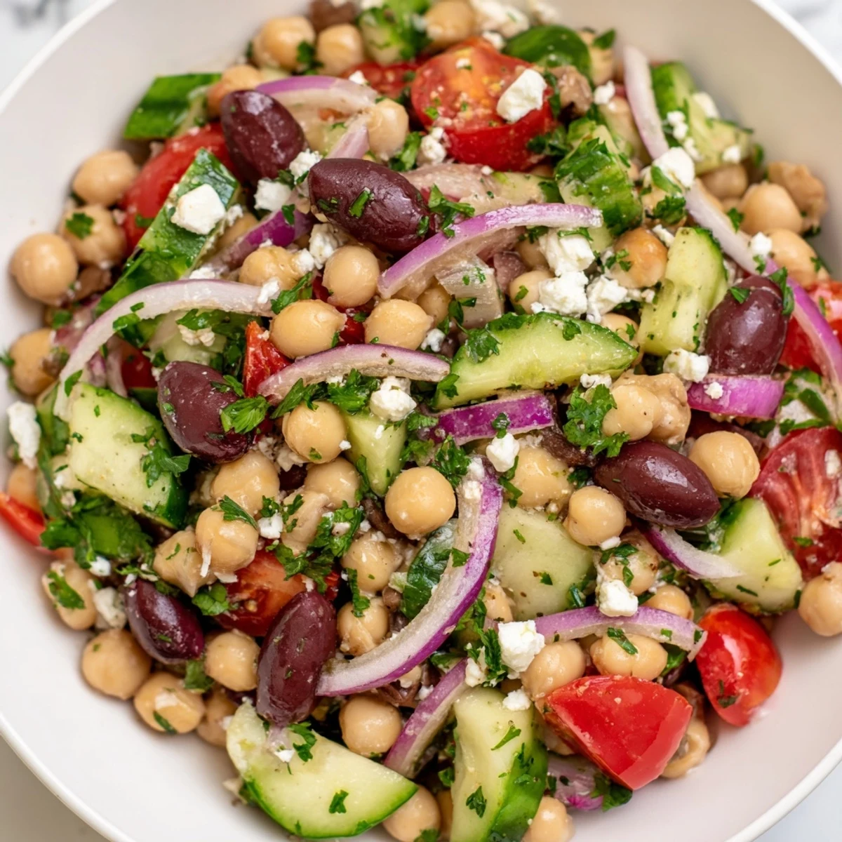 A close-up of Mediterranean Dense Bean Salad in a white bowl, showcasing chickpeas, tomatoes, and feta.