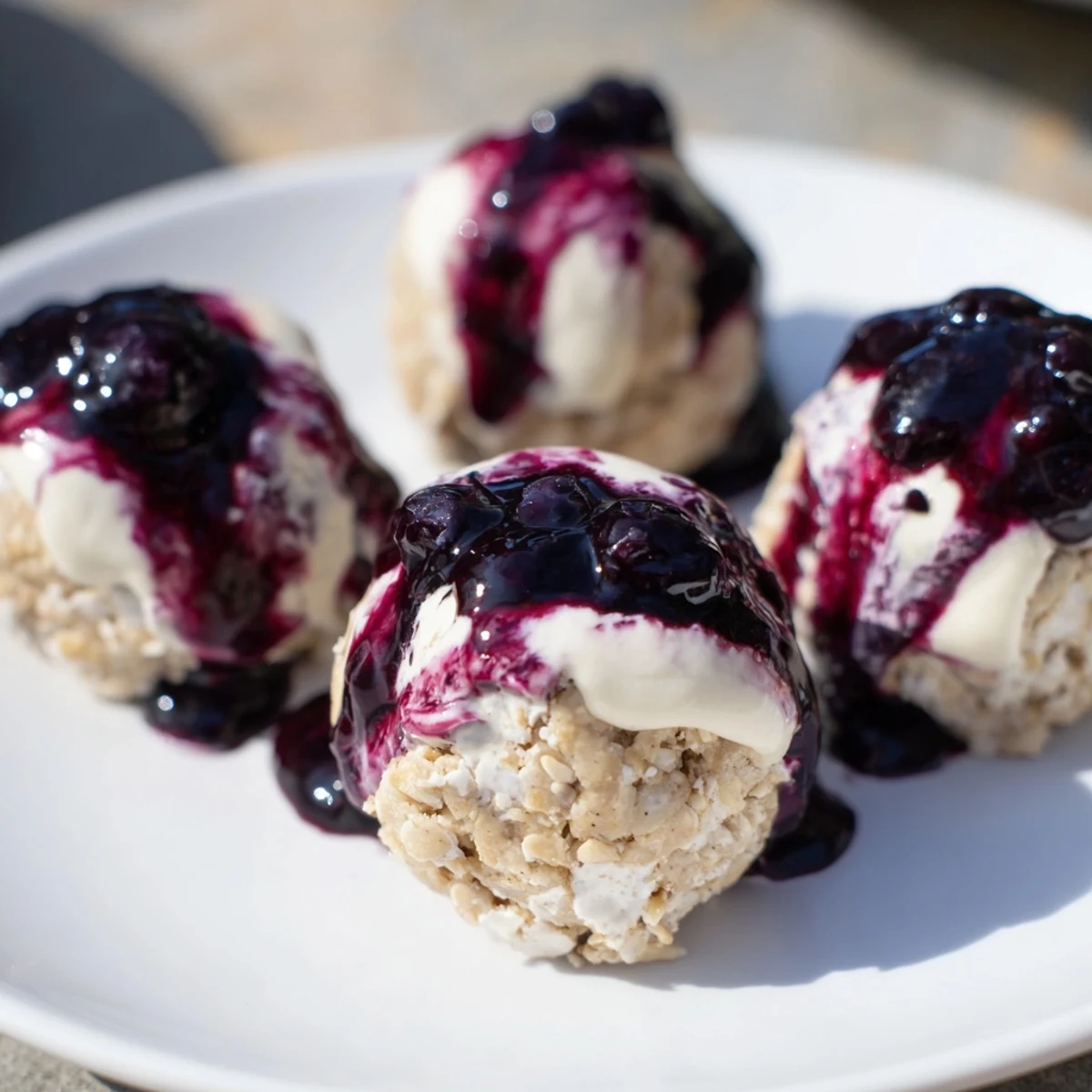 A hand reaching for a single Blueberry Cheesecake Protein Bite, revealing a dense, creamy texture and sweet blueberry compote center.