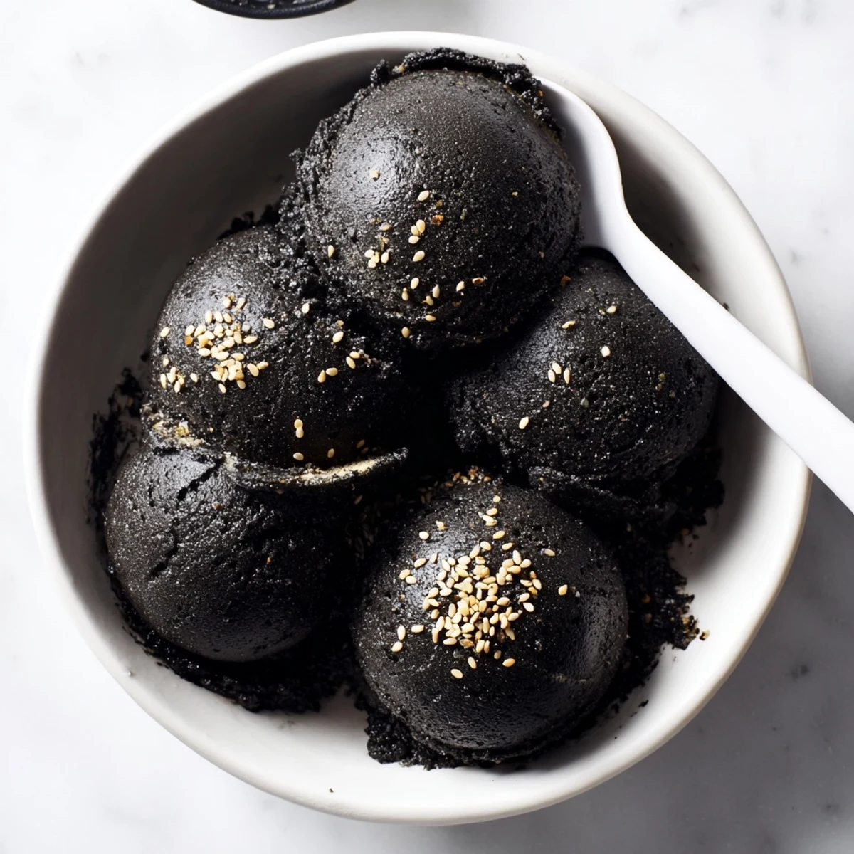 A scoop of Toasted Black Sesame Ice Cream in a chilled bowl, garnished with toasted sesame seeds.