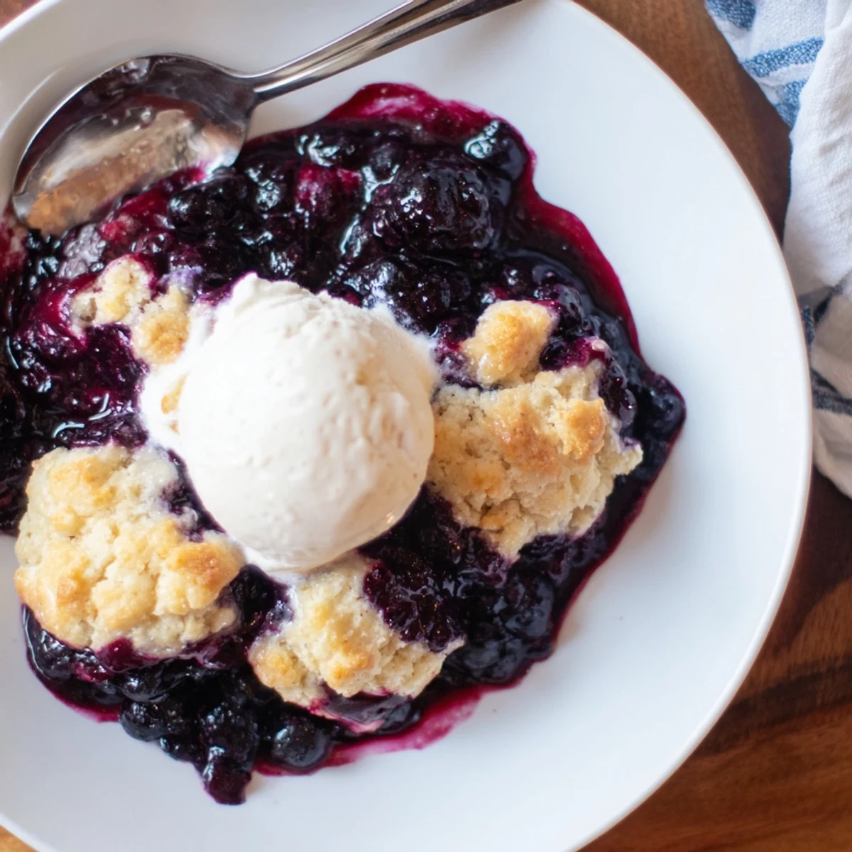 Moist Blueberry Cobbler With Frozen Berries topped with golden biscuit crumbles and bubbling blueberry filling on a rustic plate.