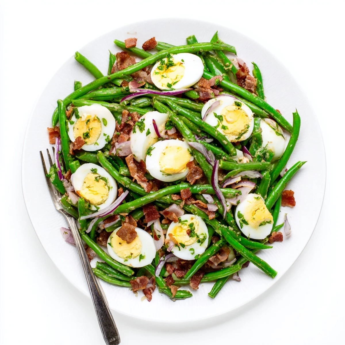 The Green Bean, Bacon, and Egg Salad sits on a white plate, featuring crunchy bacon and red onion.
