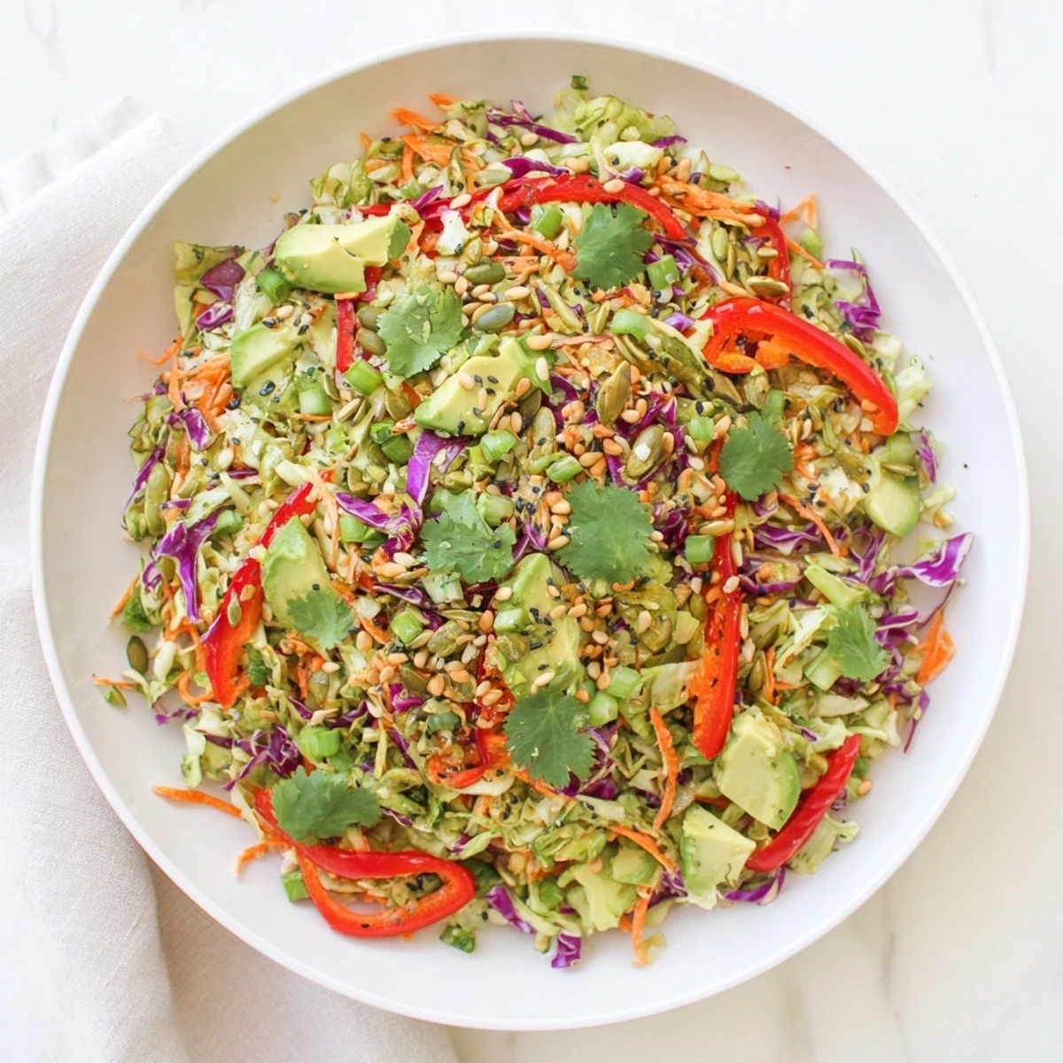 Healthy vegan Avocado Cabbage Salad served on a white plate with a garnish of green onions and cilantro leaves.