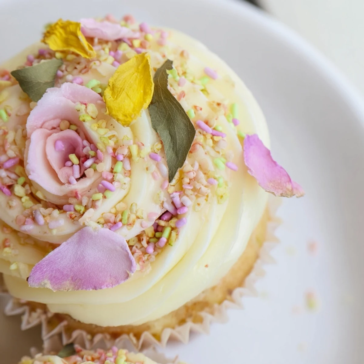 Stack of freshly baked Baby In Bloom Cupcakes topped with delicate edible pansies and pastel nonpareil sprinkles.