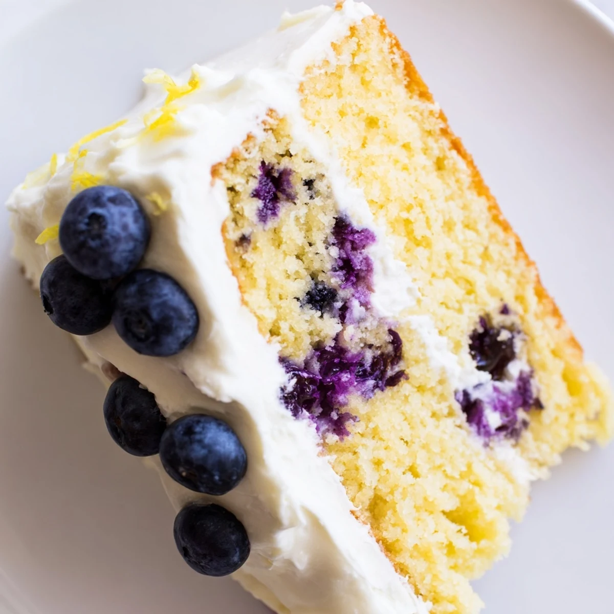 Freshly baked Lemon Blueberry Cake with Cream Cheese Frosting, vibrant blueberries dotted in golden crumbs and a thick swirl of frosting.