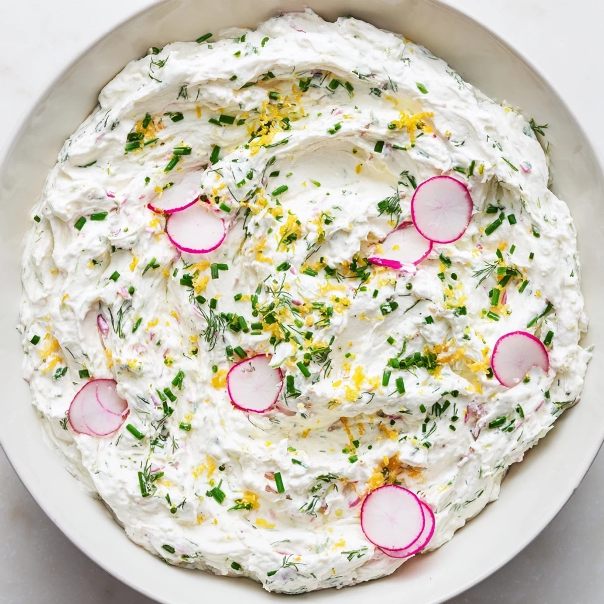 A close-up photo shows the Simple Easter Herb Cheese Dip in a white bowl, garnished with fresh chives and dill, ready for serving on a spring table.