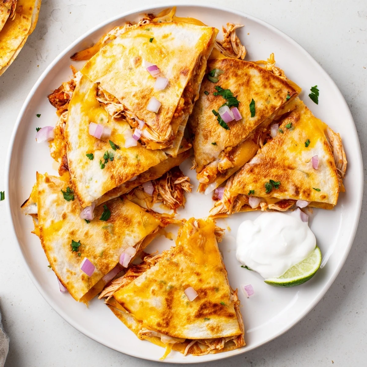 Golden-brown Hot Honey BBQ Chicken Quesadillas served with lime wedges and a dollop of cool sour cream on a rustic plate.