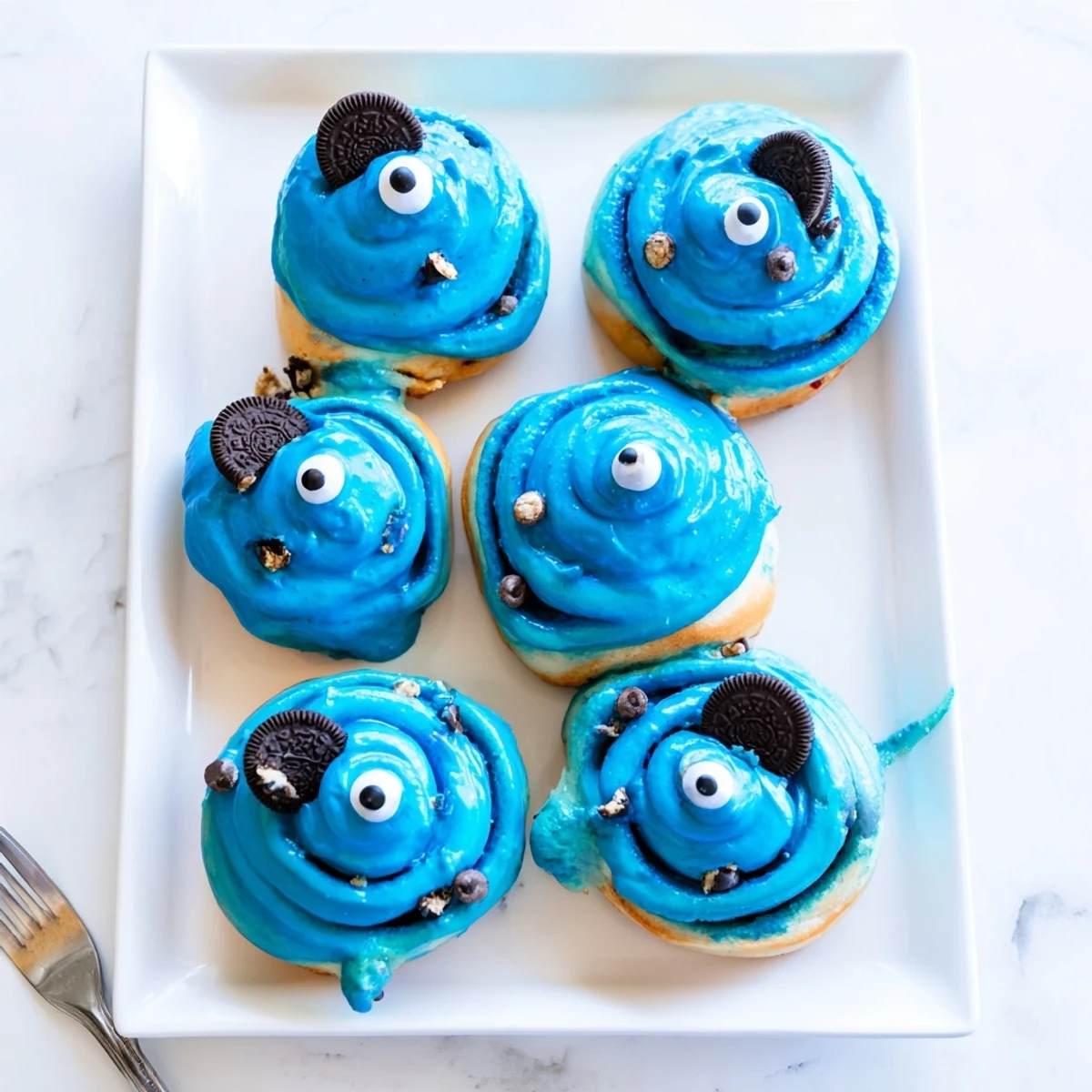 Frosted blue Cookie Monster cinnamon rolls with candy eyes sit on a cooling rack, ready for breakfast.