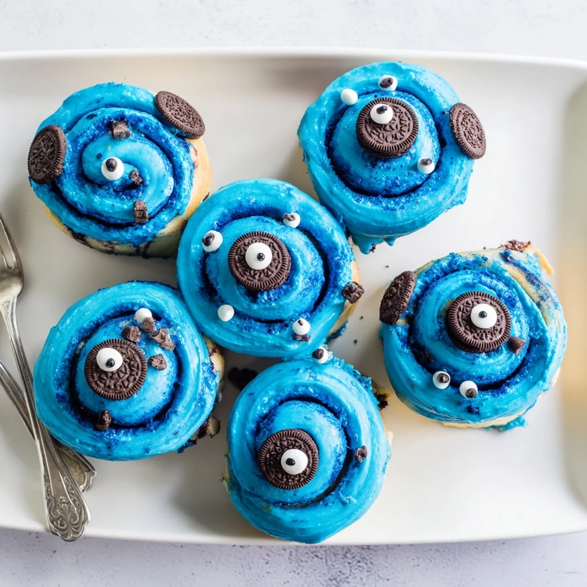 Warm Cookie Monster cinnamon rolls show swirled filling and playful cookie eyes on a white platter.