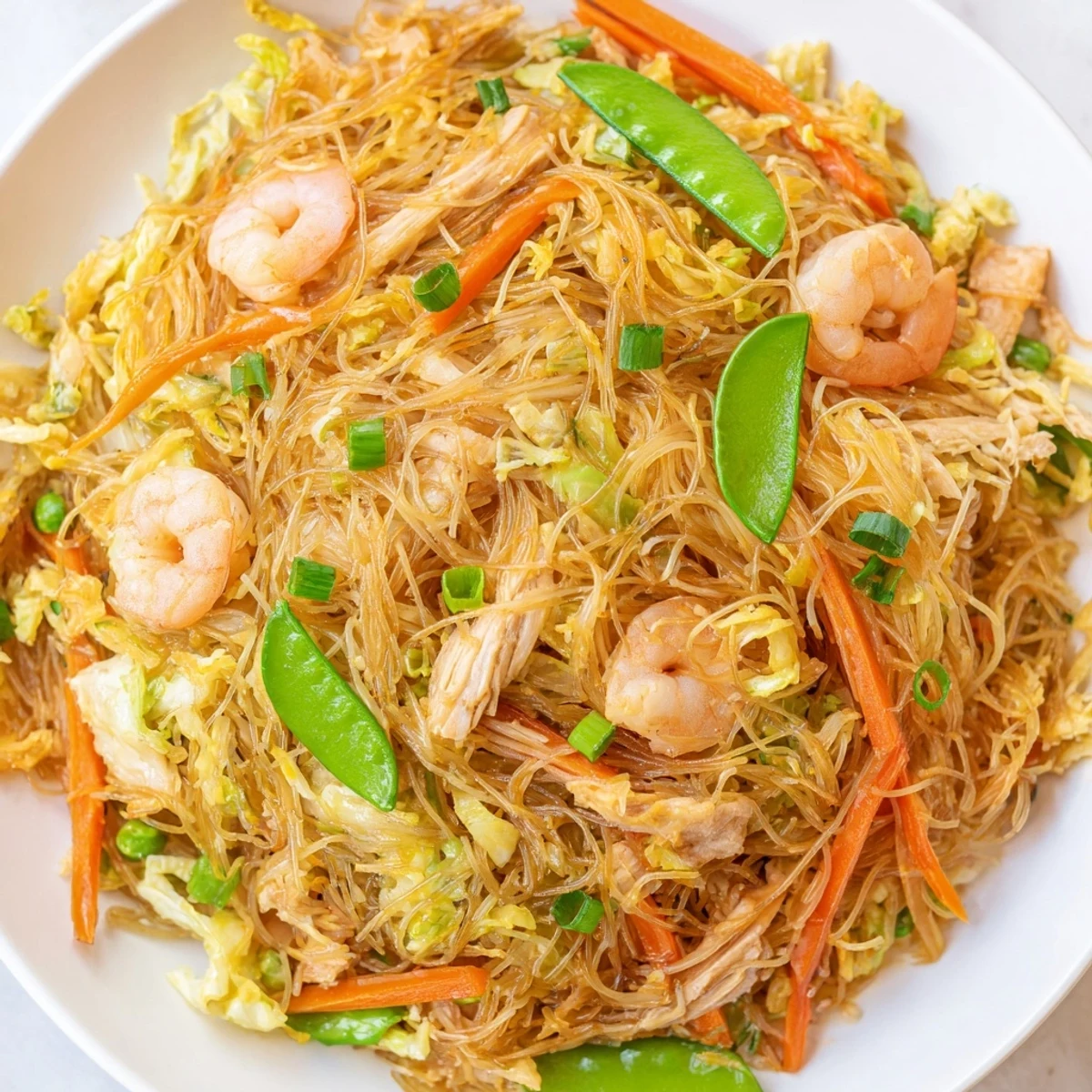 Golden mound of savory Pancit Bihon noodles topped with succulent shrimp chicken and crisp colorful vegetables