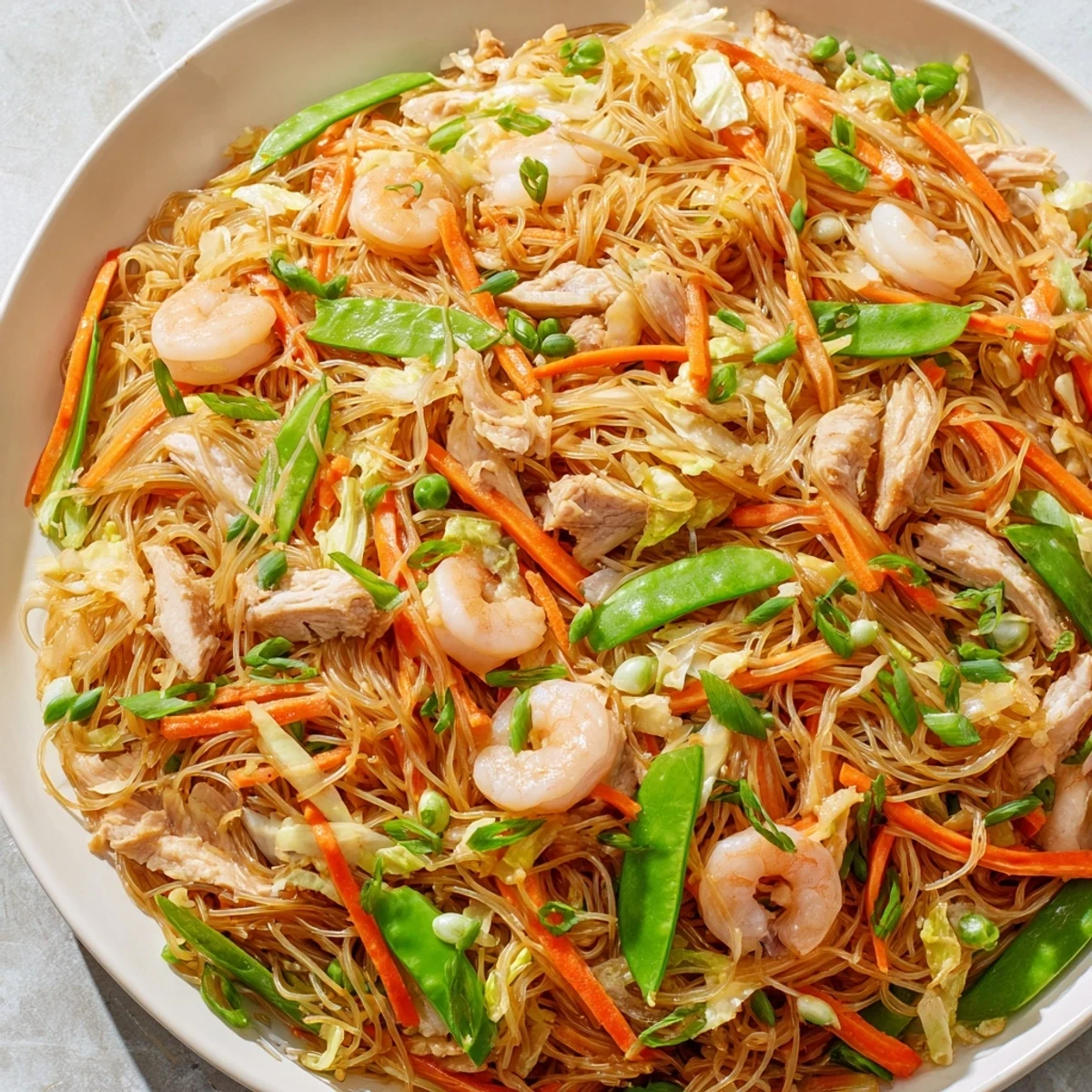 Steaming platter of traditional Pancit Bihon stir-fried rice noodles garnished with fresh scallions and citrus wedges