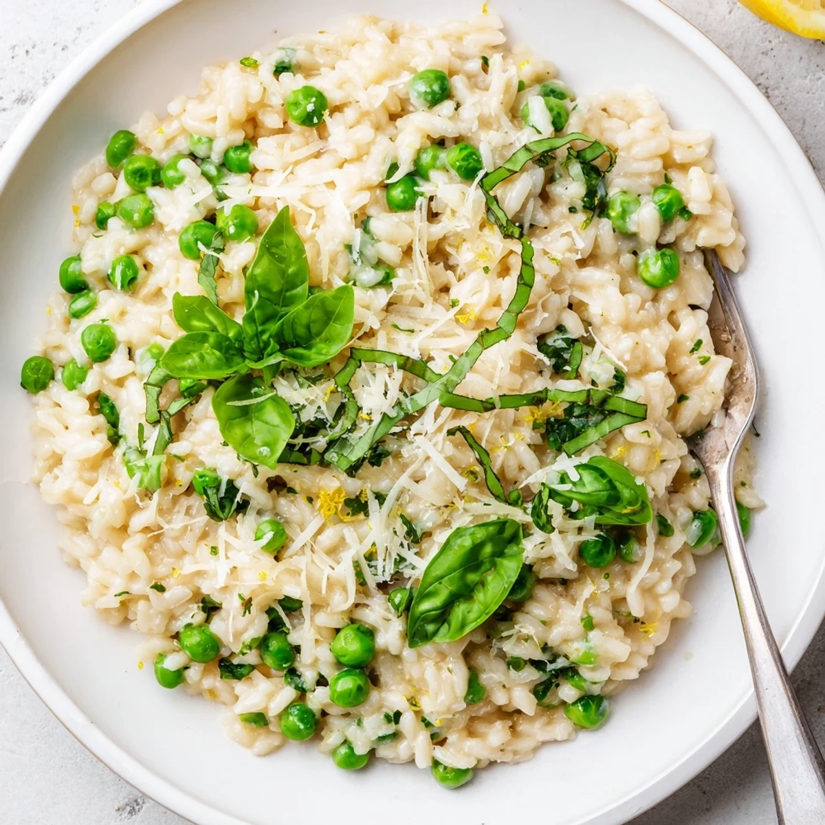 Creamy spring pea risotto topped with fresh basil and grated Parmesan cheese in a white bowl