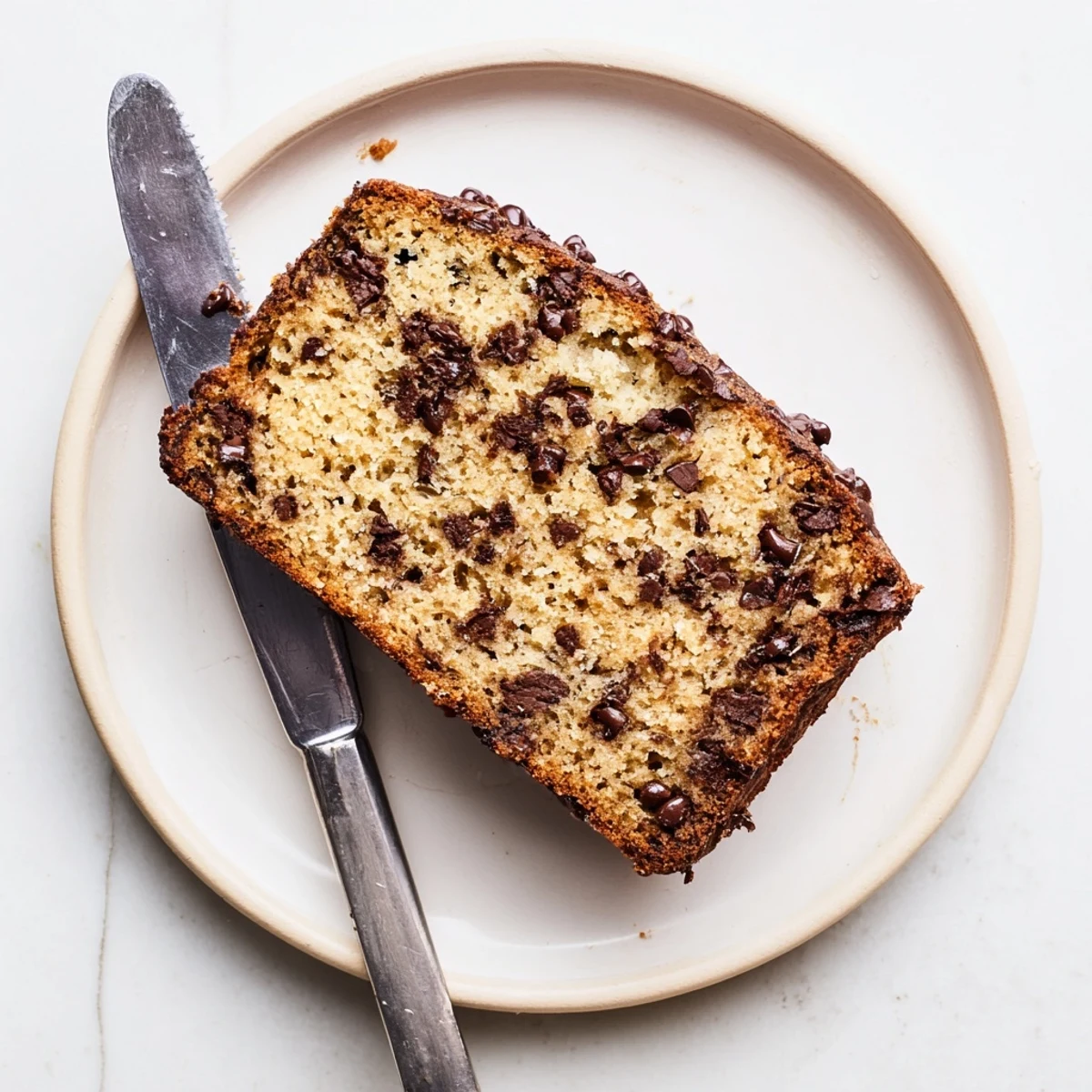 Golden brown classic chocolate chip banana bread loaf studded with melted chocolate chunks on a rustic wooden cutting board