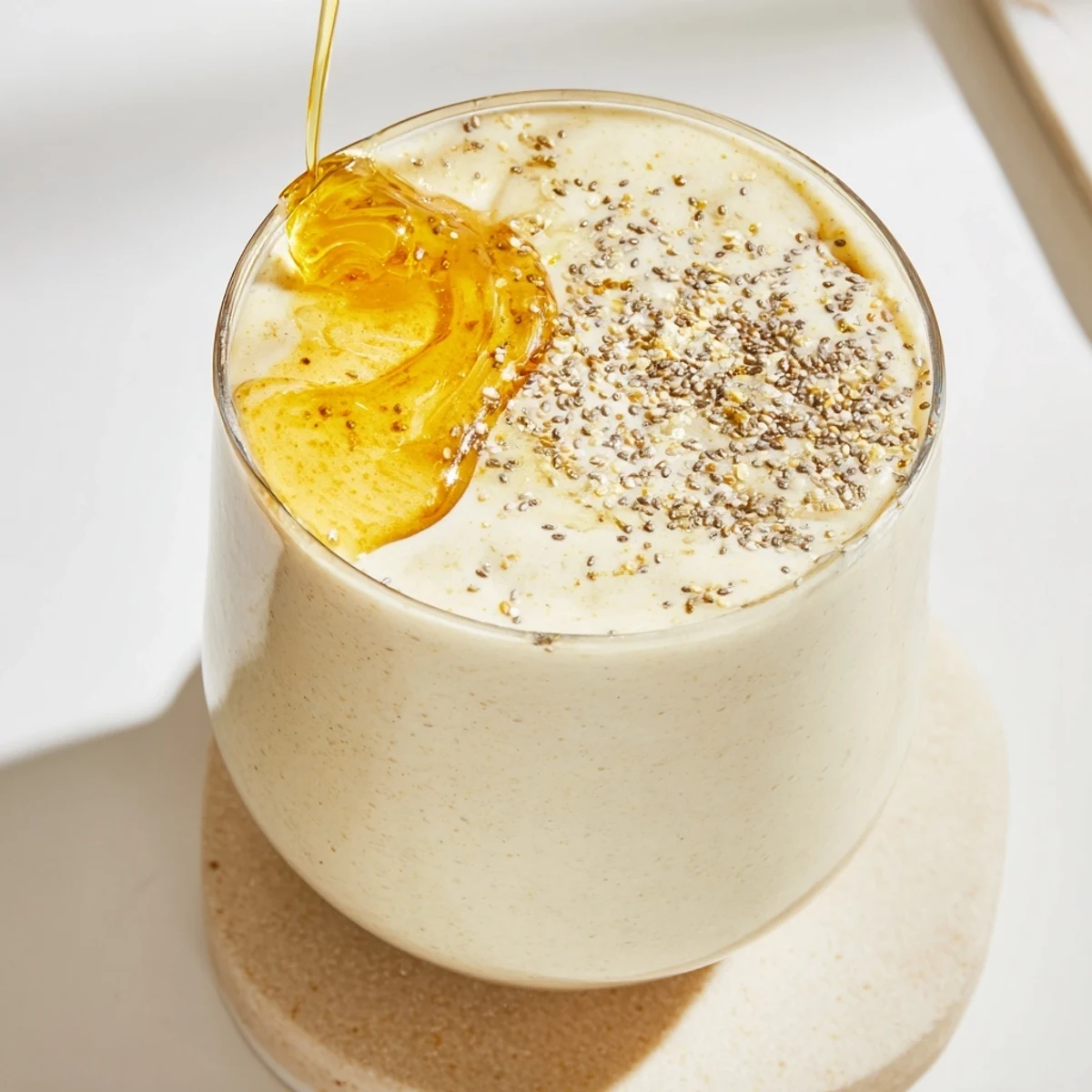 Golden Greek yogurt banana smoothie with ice swirls served with whole banana on the side