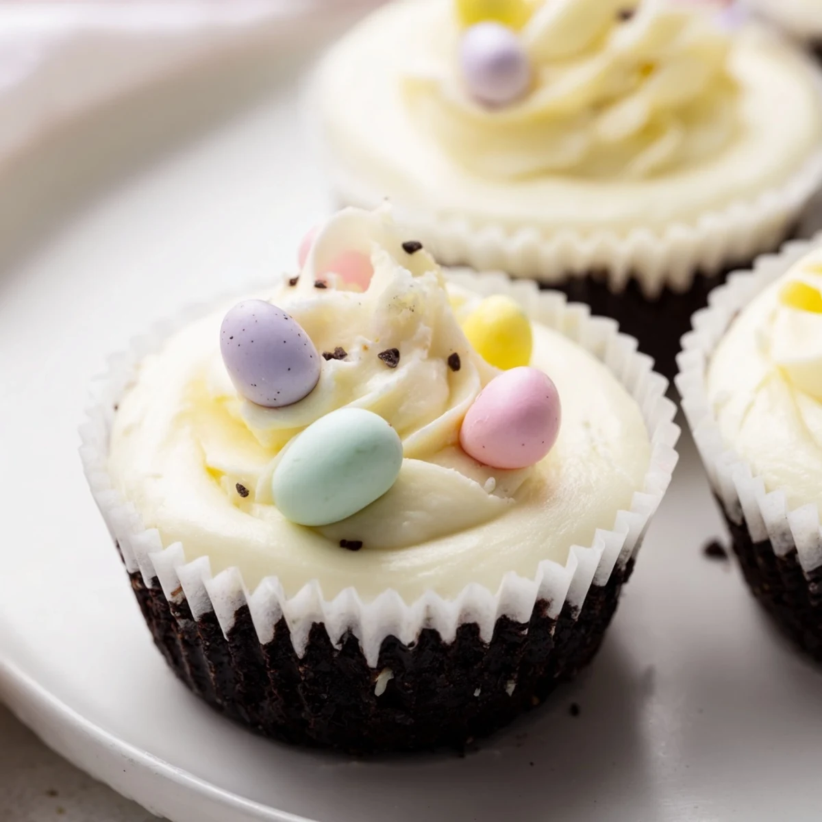 Golden mini cheesecakes topped with whipped cream and colorful Cadbury Mini Eggs on chocolate cookie crusts