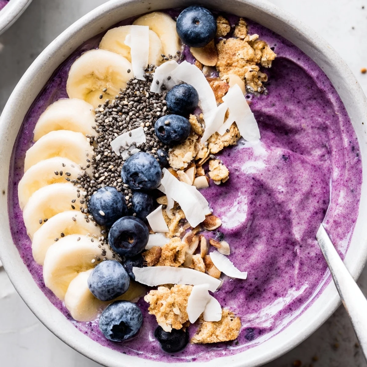 Spoon ready to enjoy this purple blueberry smoothie bowl with Greek yogurt and colorful fruit arranging