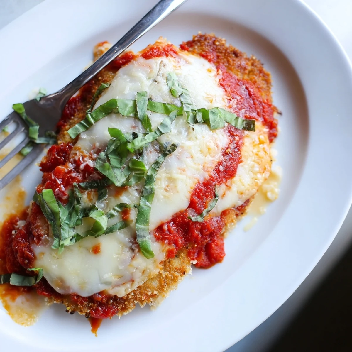 Crispy almond flour crusted chicken Parmigiana topped with fresh basil garnish and gooey cheese under warm oven lighting