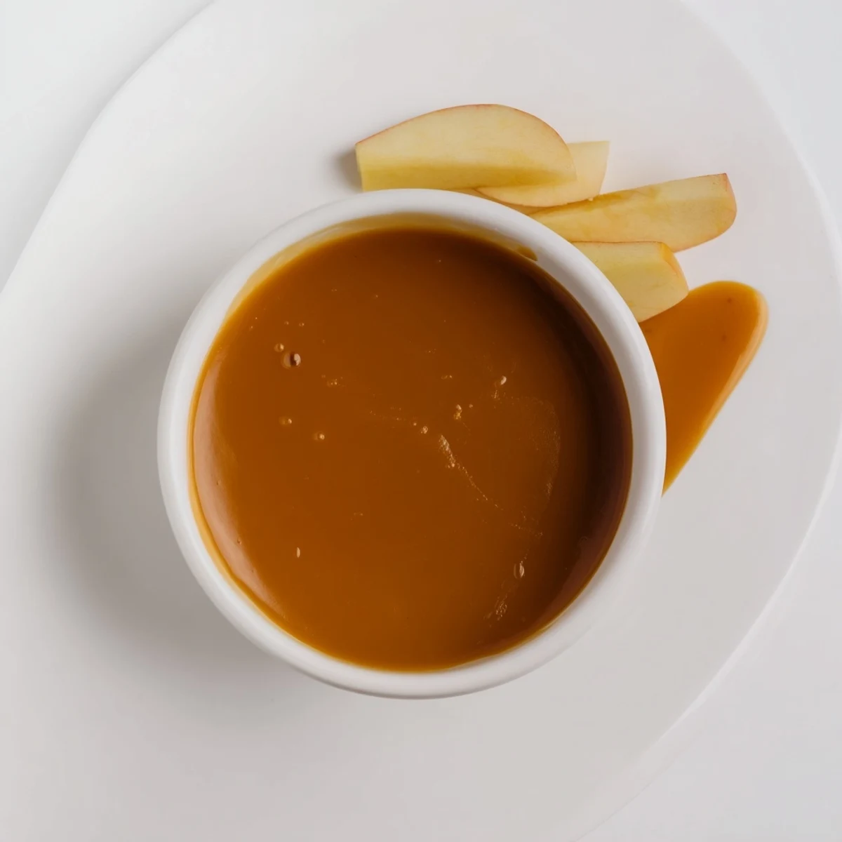 Silky homemade easy caramel sauce swirling from a wooden spoon against dark background