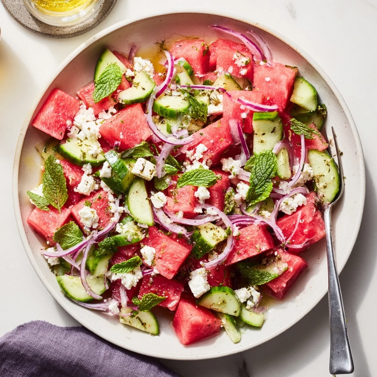 Fresh watermelon feta salad bowl with juicy red cubes, cucumber, mint leaves, and white crumbled cheese topping