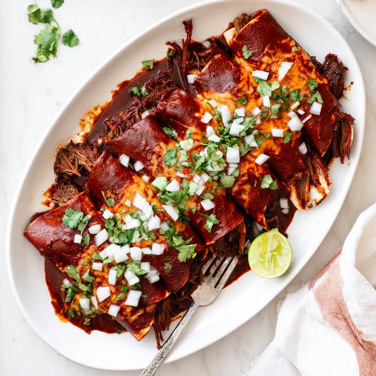Tender shredded beef birria enchiladas smothered in rich consommé with bubbling Oaxaca cheese