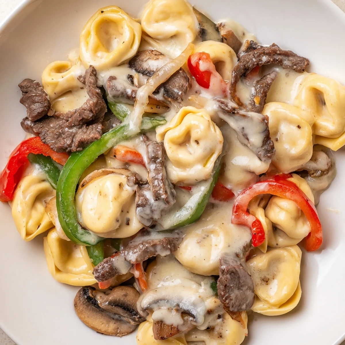 Slow cooker cheesesteak tortellini dish with seared beef strips, sautéed vegetables, and cheesy tortellini swimming in a garlic-infused cream broth