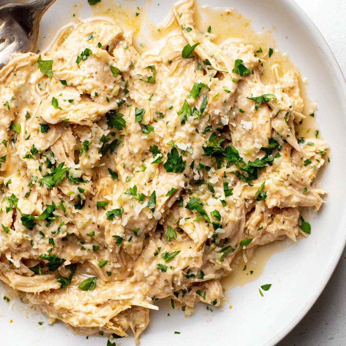 Golden Crockpot creamy garlic Parmesan chicken garnished with fresh parsley and served over mashed potatoes