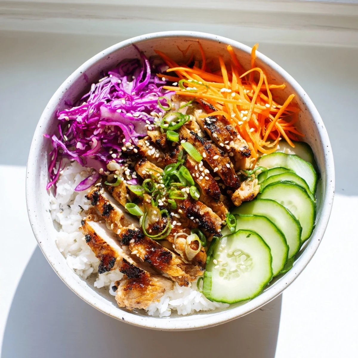 Golden glazed Korean BBQ chicken sliced over fluffy rice with crisp purple cabbage and cucumbers