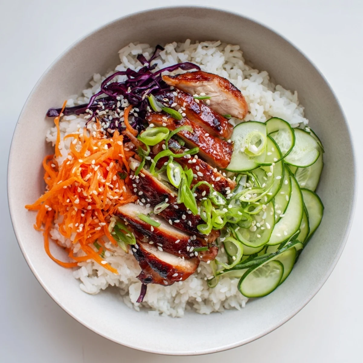 Juicy grilled Korean BBQ chicken pieces arranged with shredded carrots, cucumber slices, and sesame seed toppings