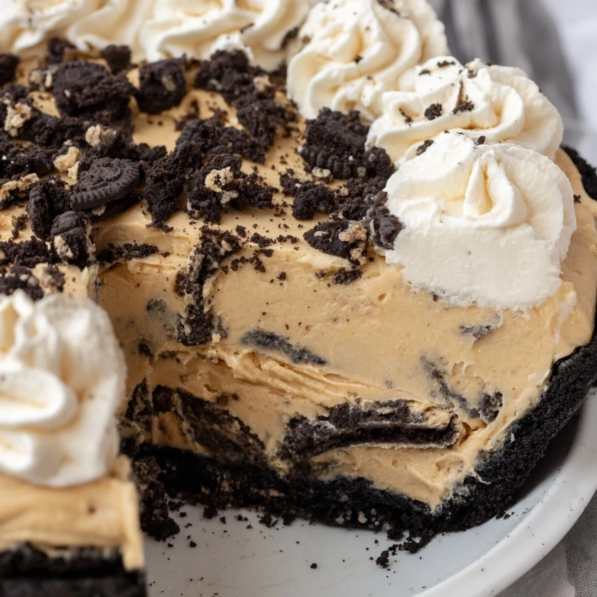 Creamy peanut butter Oreo pie topped with fluffy whipped cream and chocolate cookie crumbles