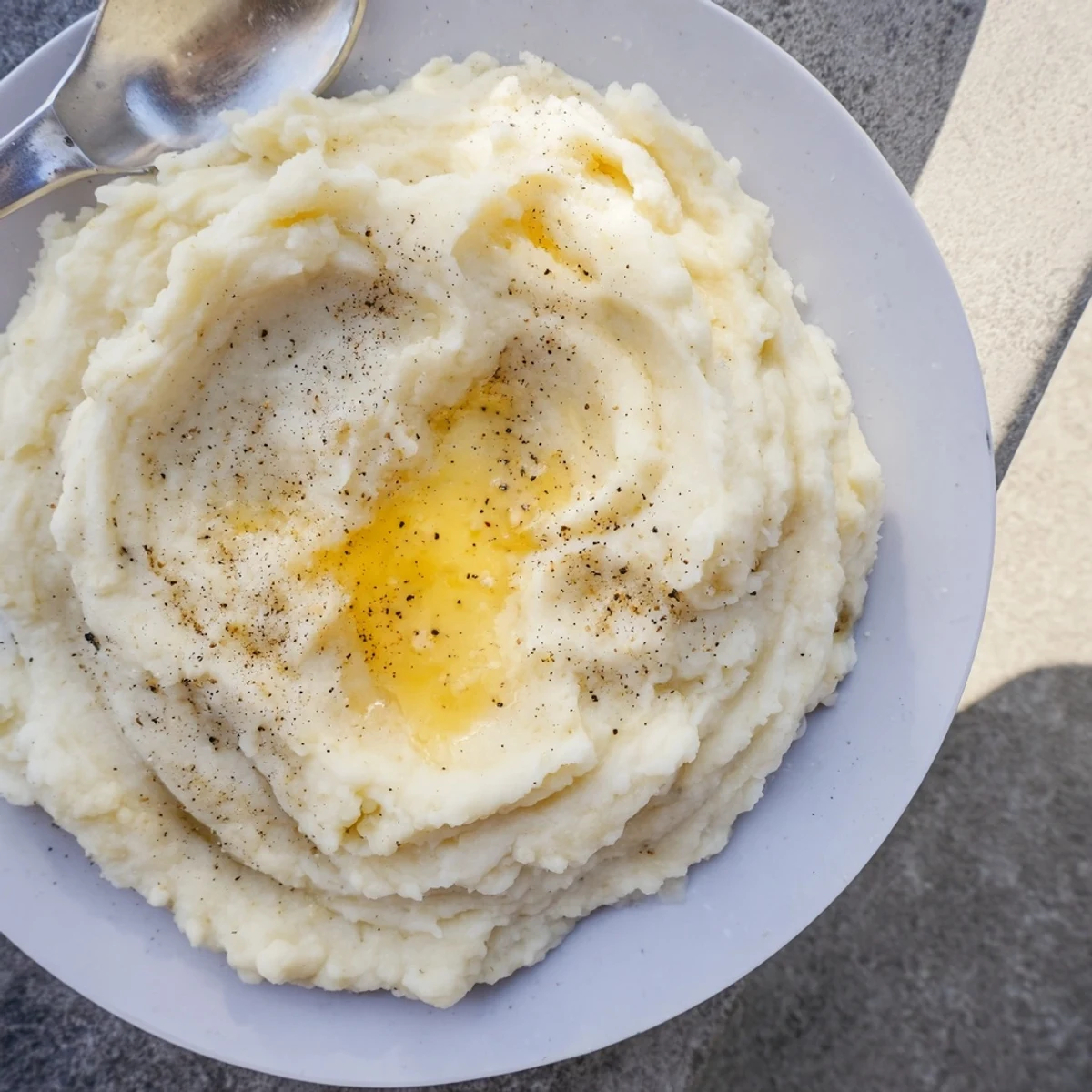 Fluffy buttery mashed potatoes in a ceramic bowl with black pepper sprinkled on top