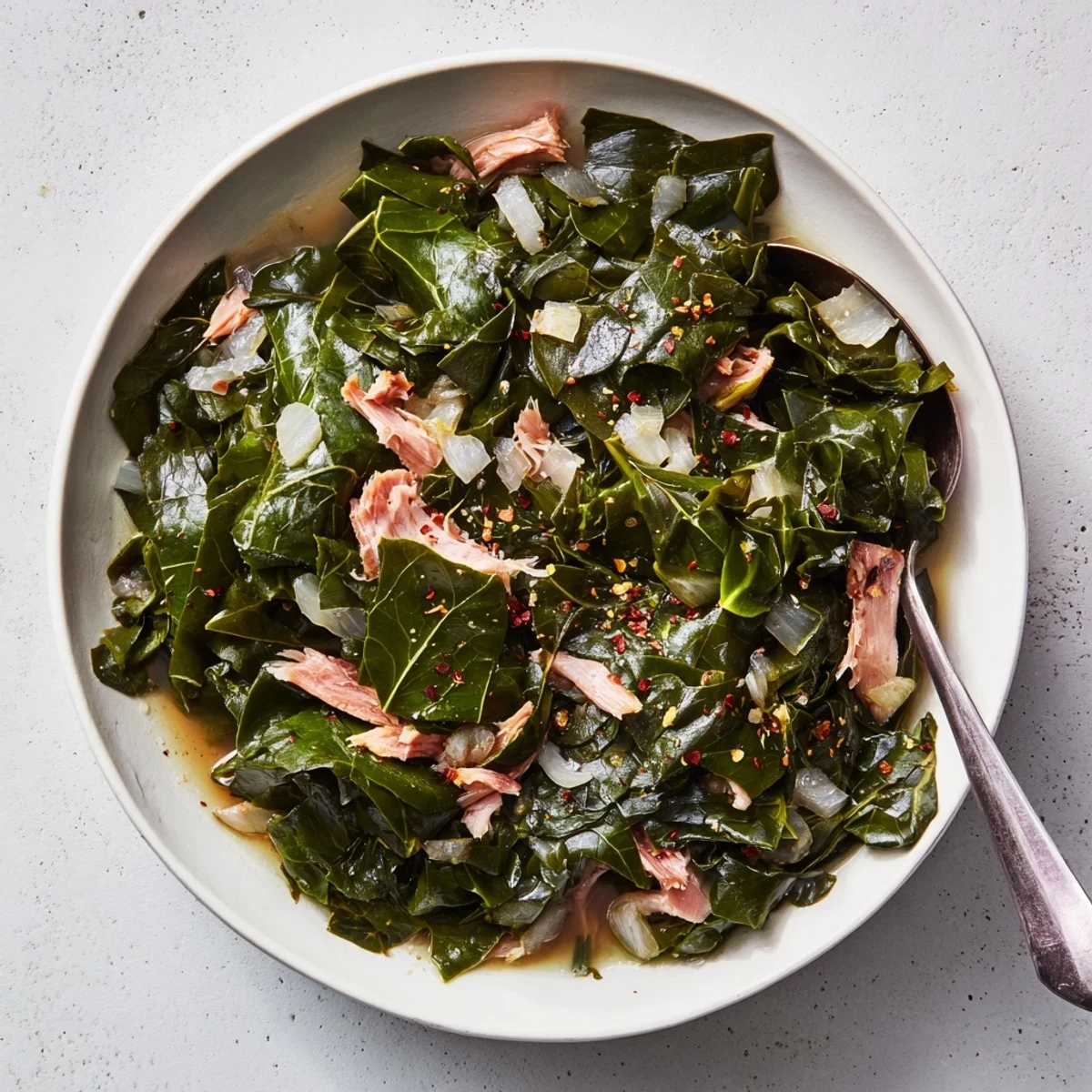 Slow-cooked collard greens recipe served in a white bowl alongside golden cornbread