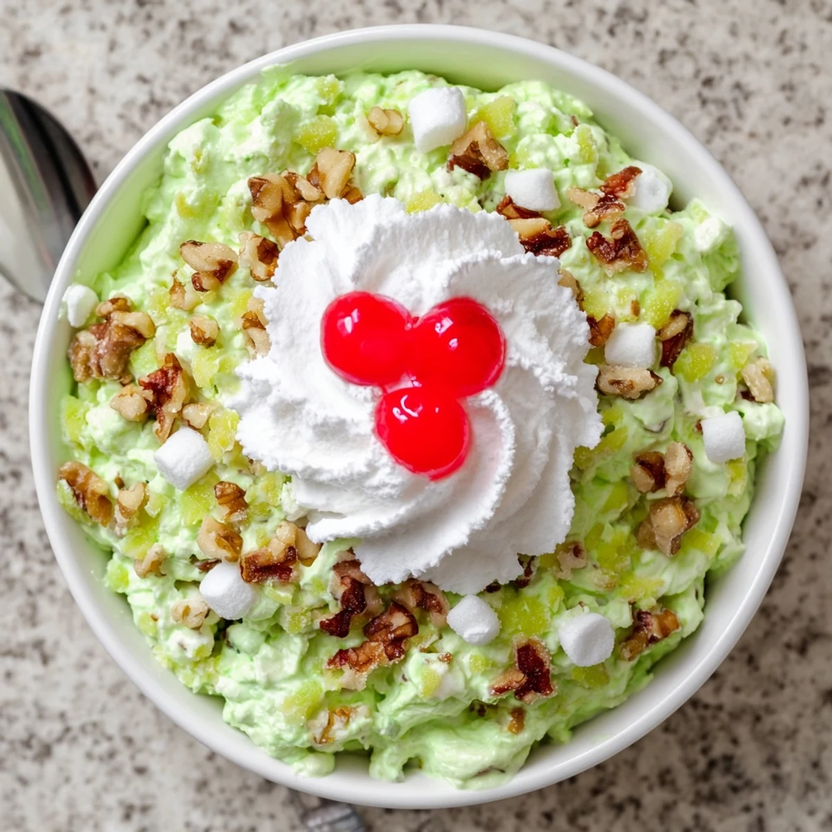 Vintage Watergate Salad dessert speckled with chopped walnuts and garnished with maraschino cherries for a festive potluck presentation