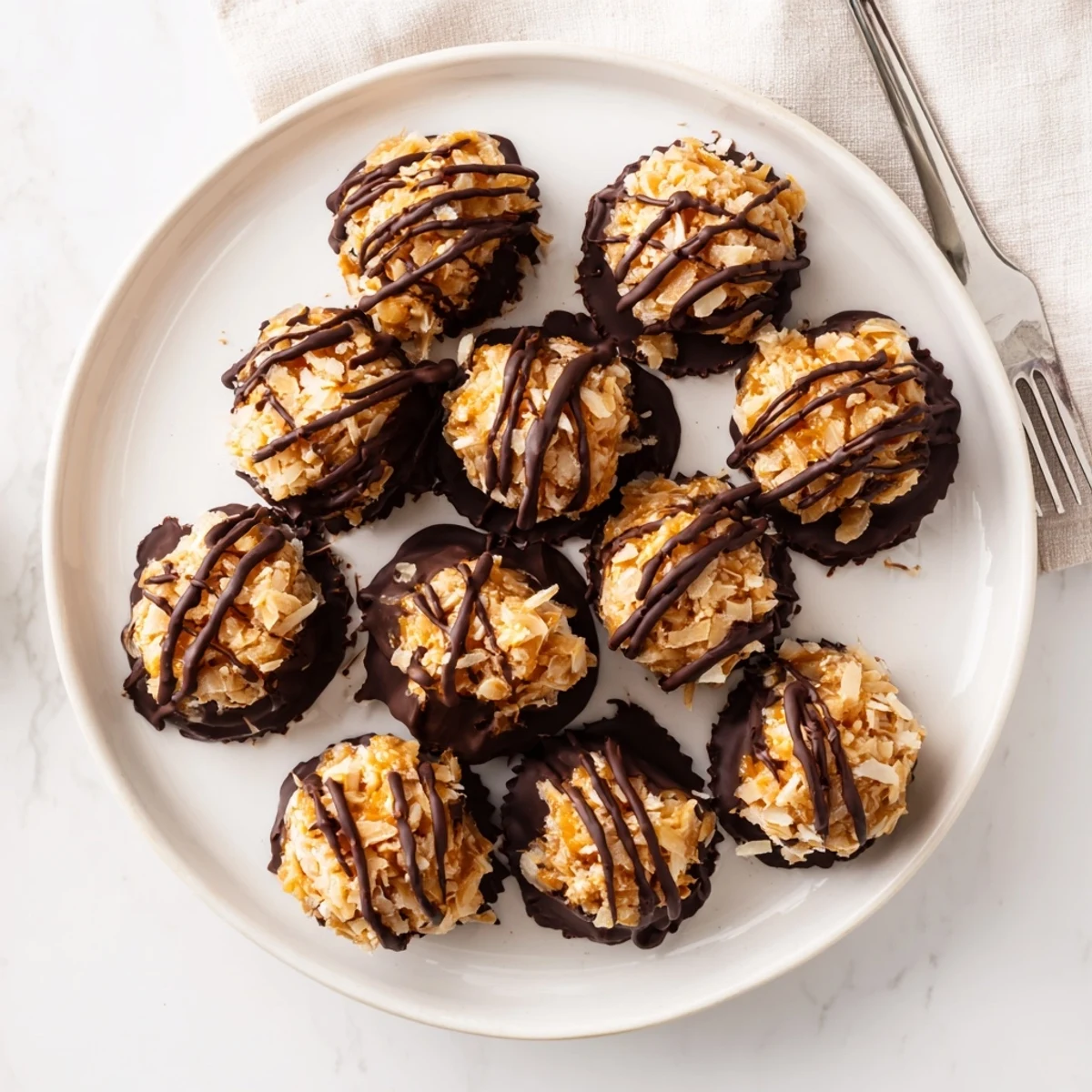 No bake Samoa bites stacked on a white plate with chocolate drizzle and toasted coconut flakes