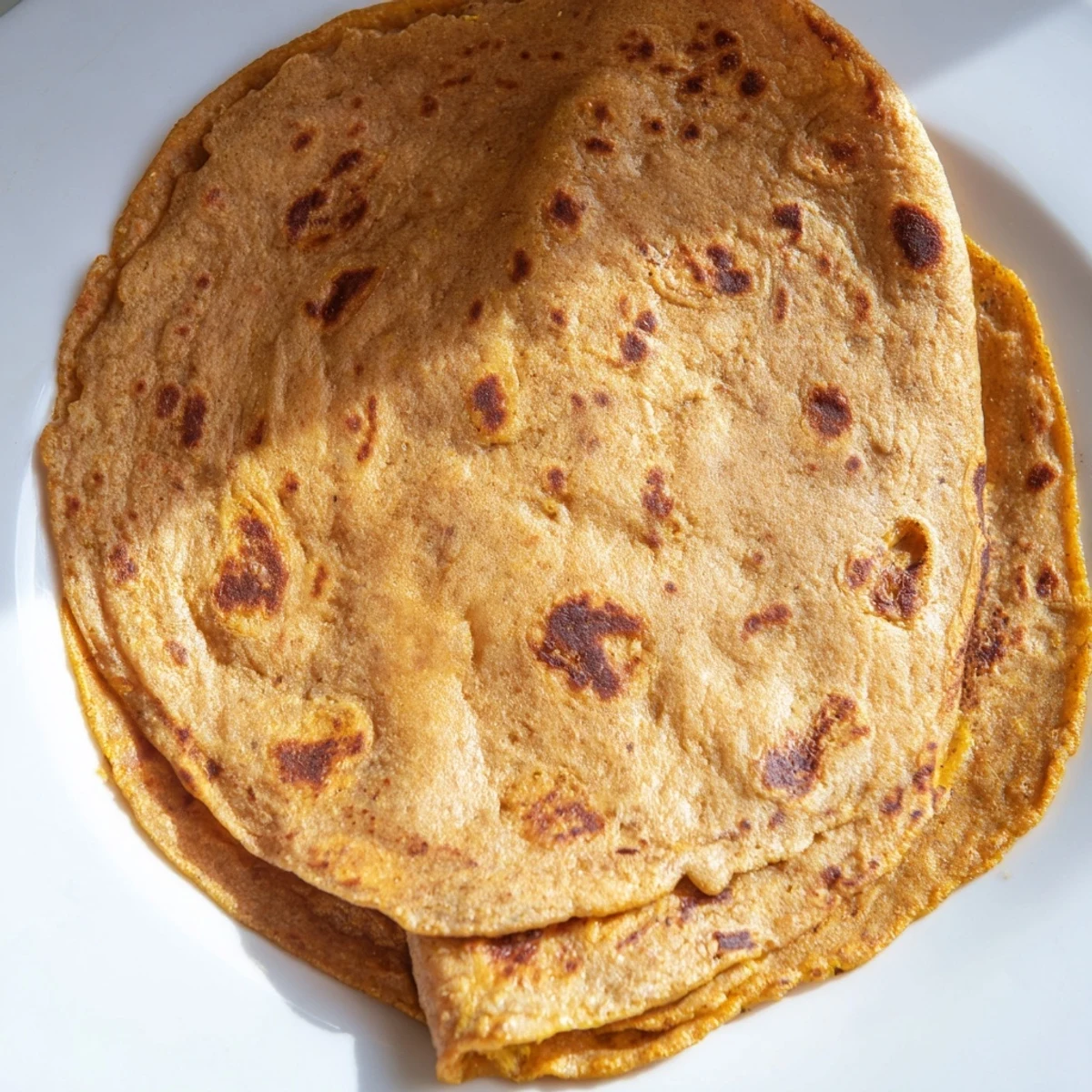 Golden brown sweet potato cassava tortillas stacked on a wooden cutting board, soft and pliable with light char marks