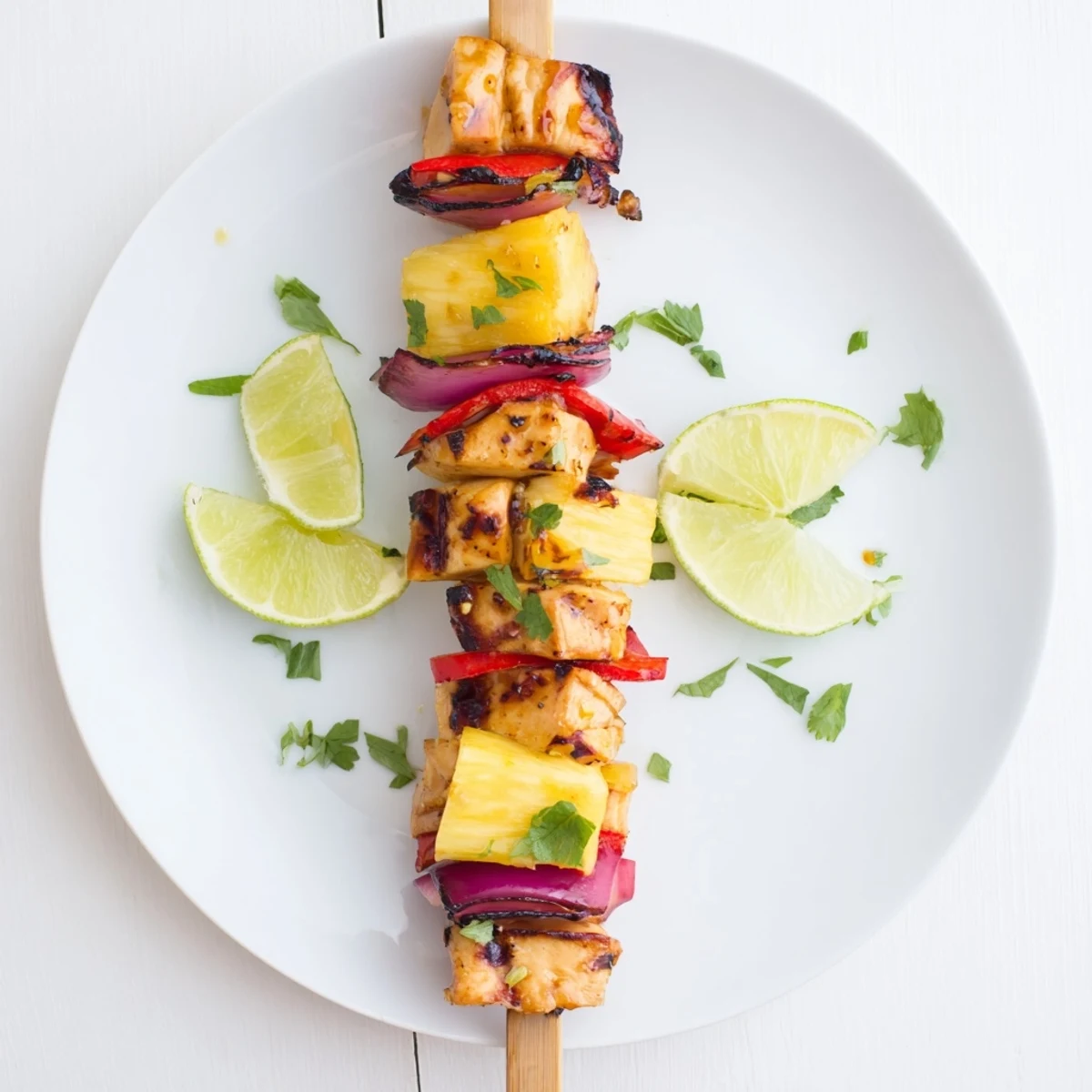 Grilled Pineapple Chicken Kabobs glistening with charred edges, served with lime wedges.