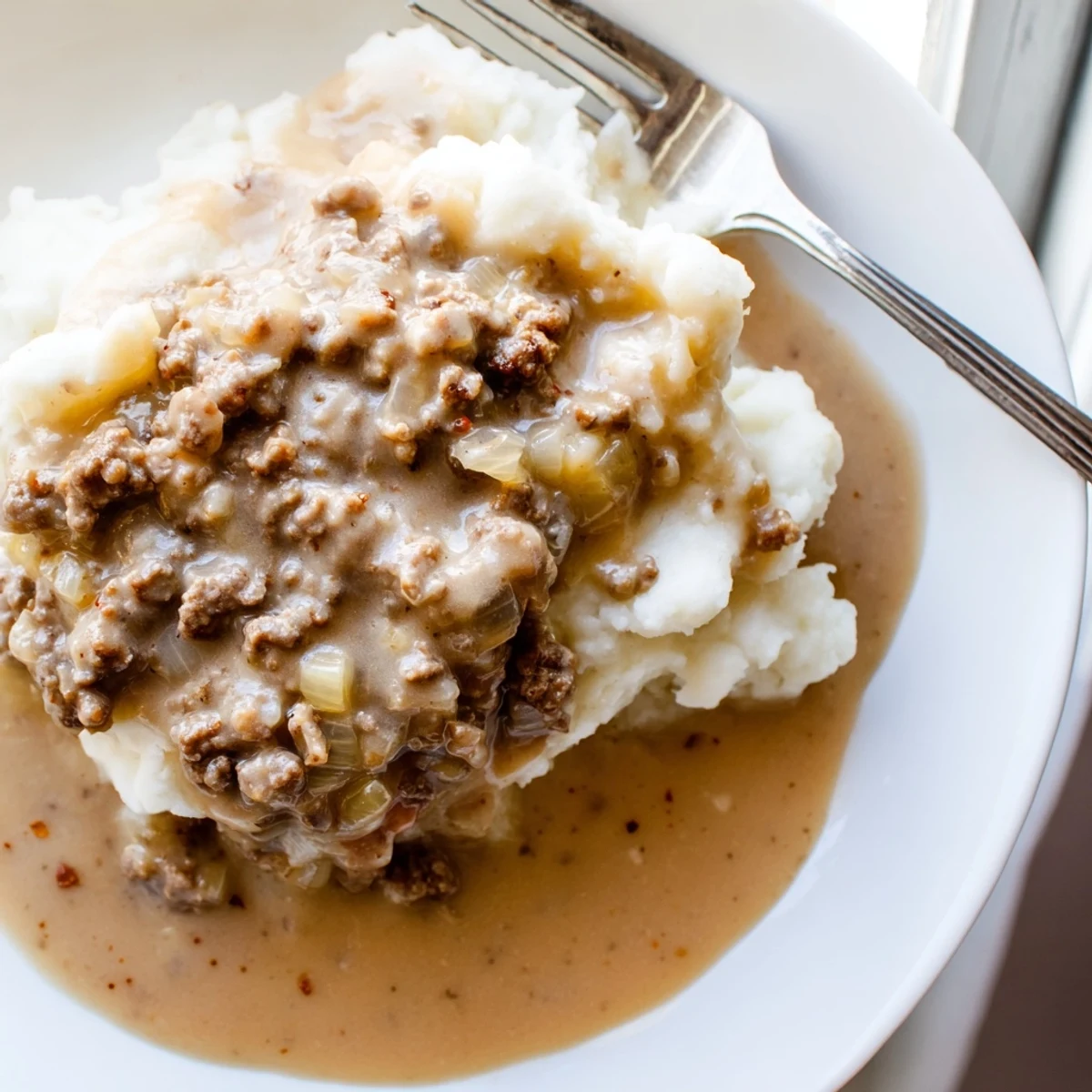 Rich brown homemade hamburger gravy spooned over steaming white rice garnished with fresh parsley