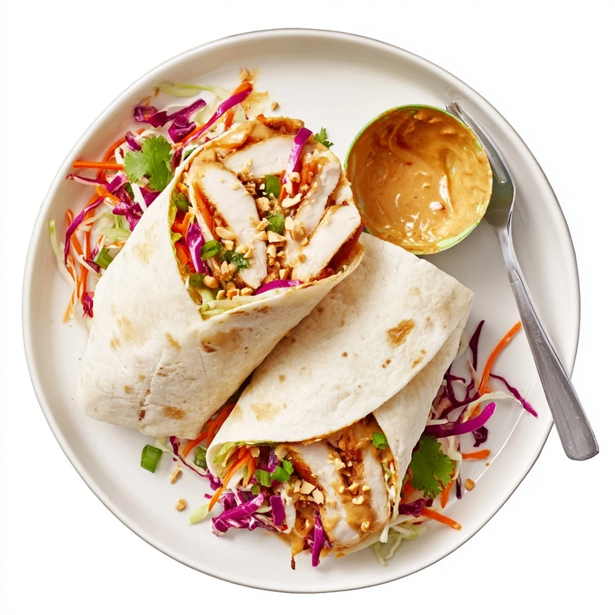 Handheld Thai Peanut Chicken Wraps served on plate, garnished with cilantro and chopped peanuts.