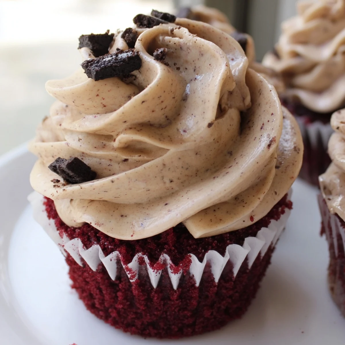 Soft red velvet Oreo cupcakes with swirls of tangy cream cheese frosting and scattered crumbs