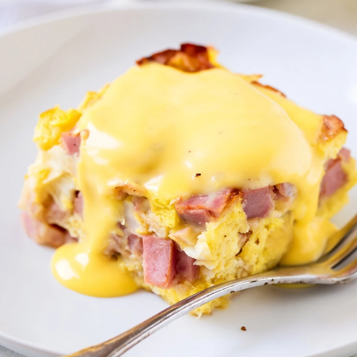 Sliced Eggs Benedict casserole drizzled with hollandaise on a white serving plate